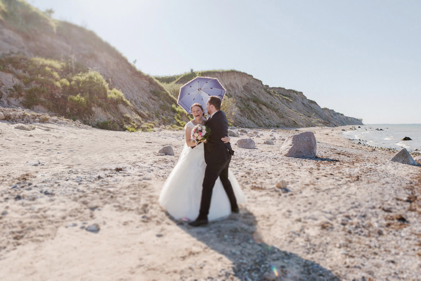 lachendes Brautpaar mit Sonnenschirm am Strand