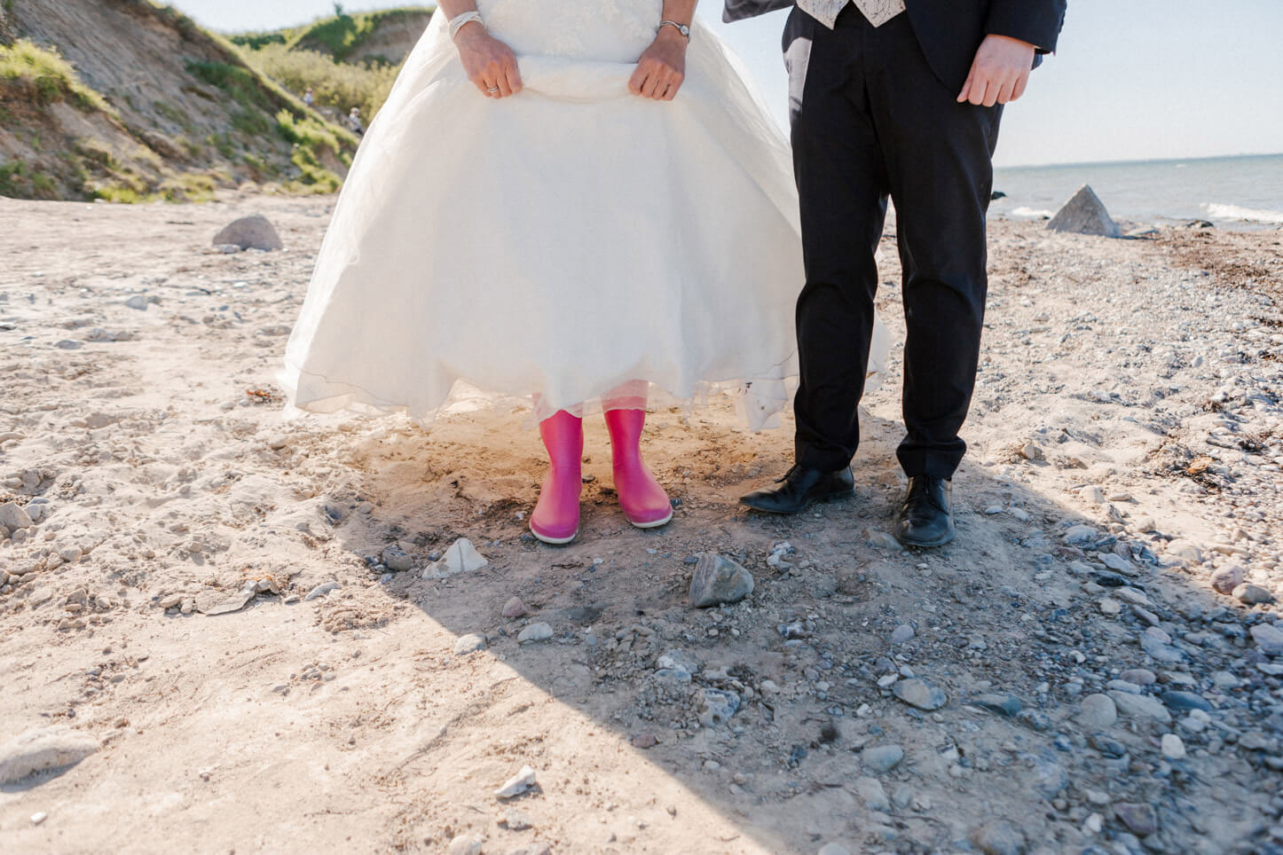 Braut mit rosa Gummistiefeln am Strand